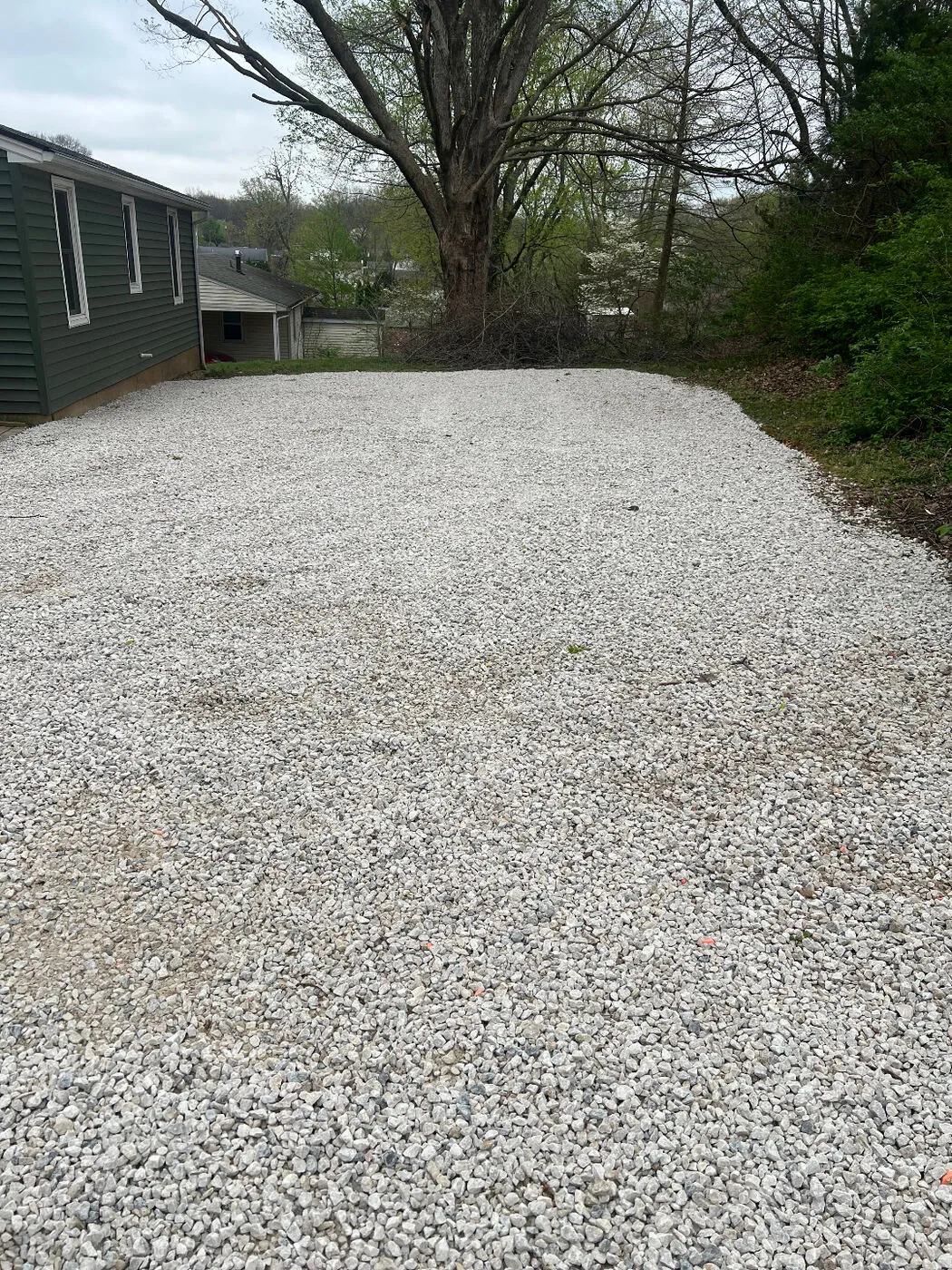 Wide gravel parking pad poured and leveled in a residential backyard.
