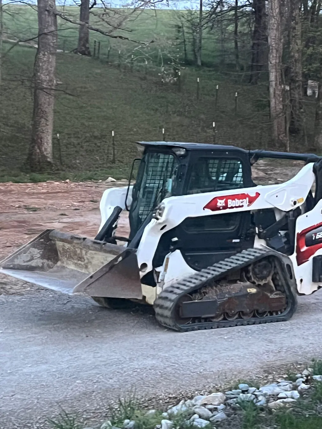Bobcat T66 compact track loader on site at the edge of a rural property.