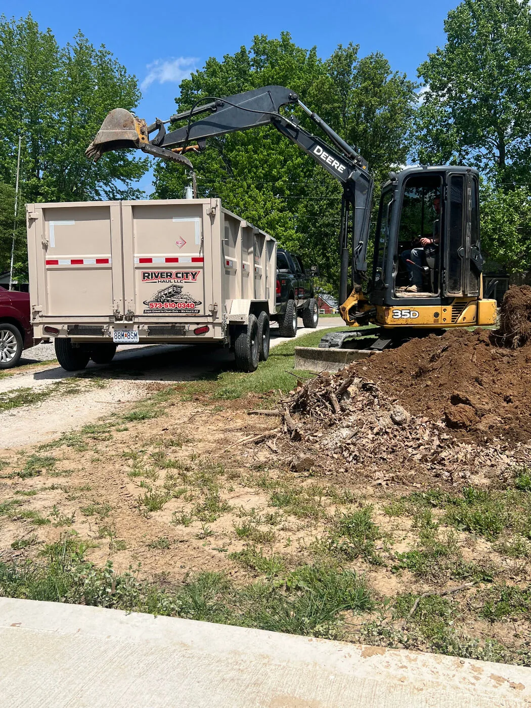 Mini excavator working alongside a loaded dump trailer on a residential clean-out job.