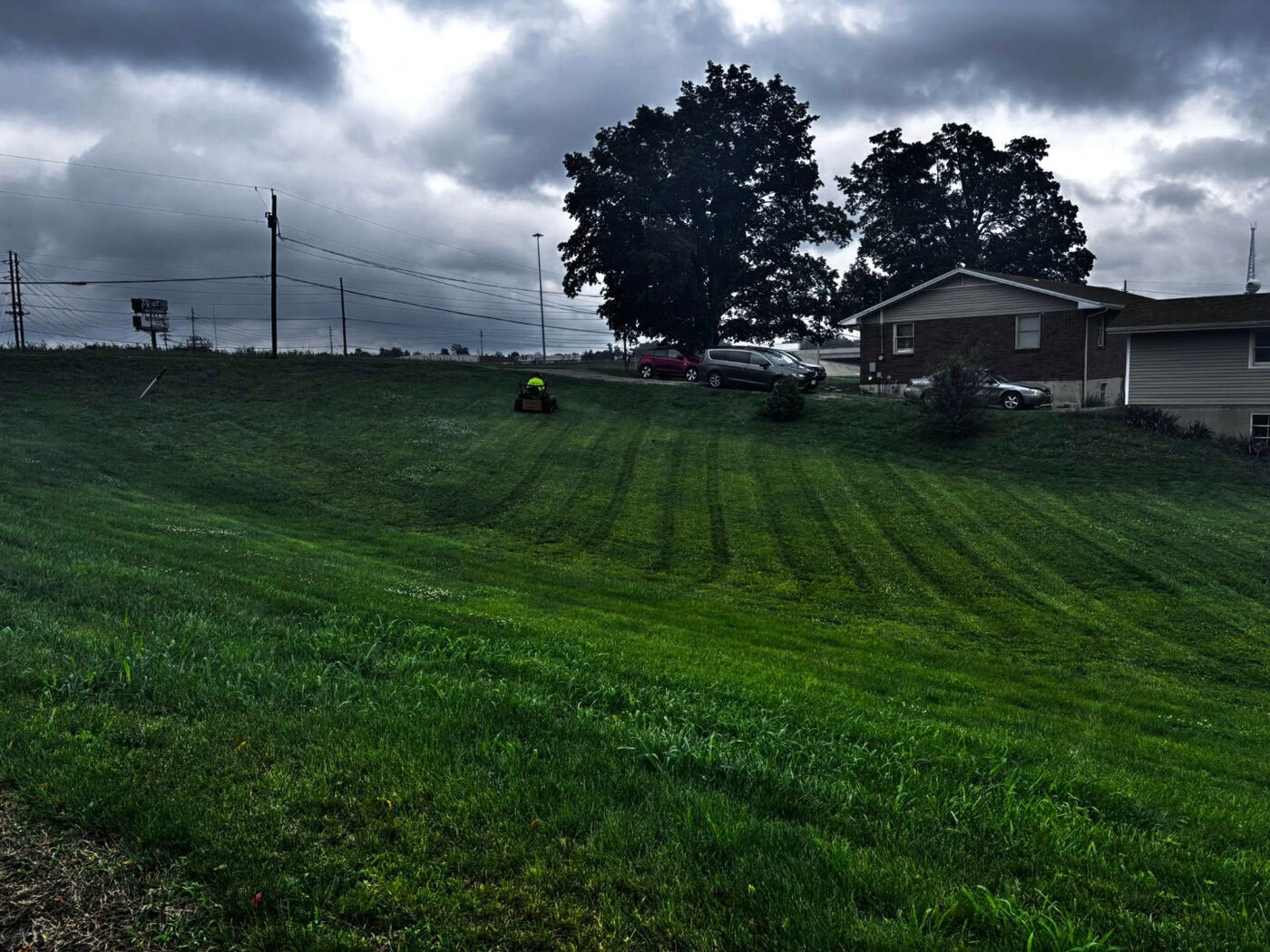 Freshly mowed hillside lawn on a cloudy day with a zero-turn mower and houses in the background.