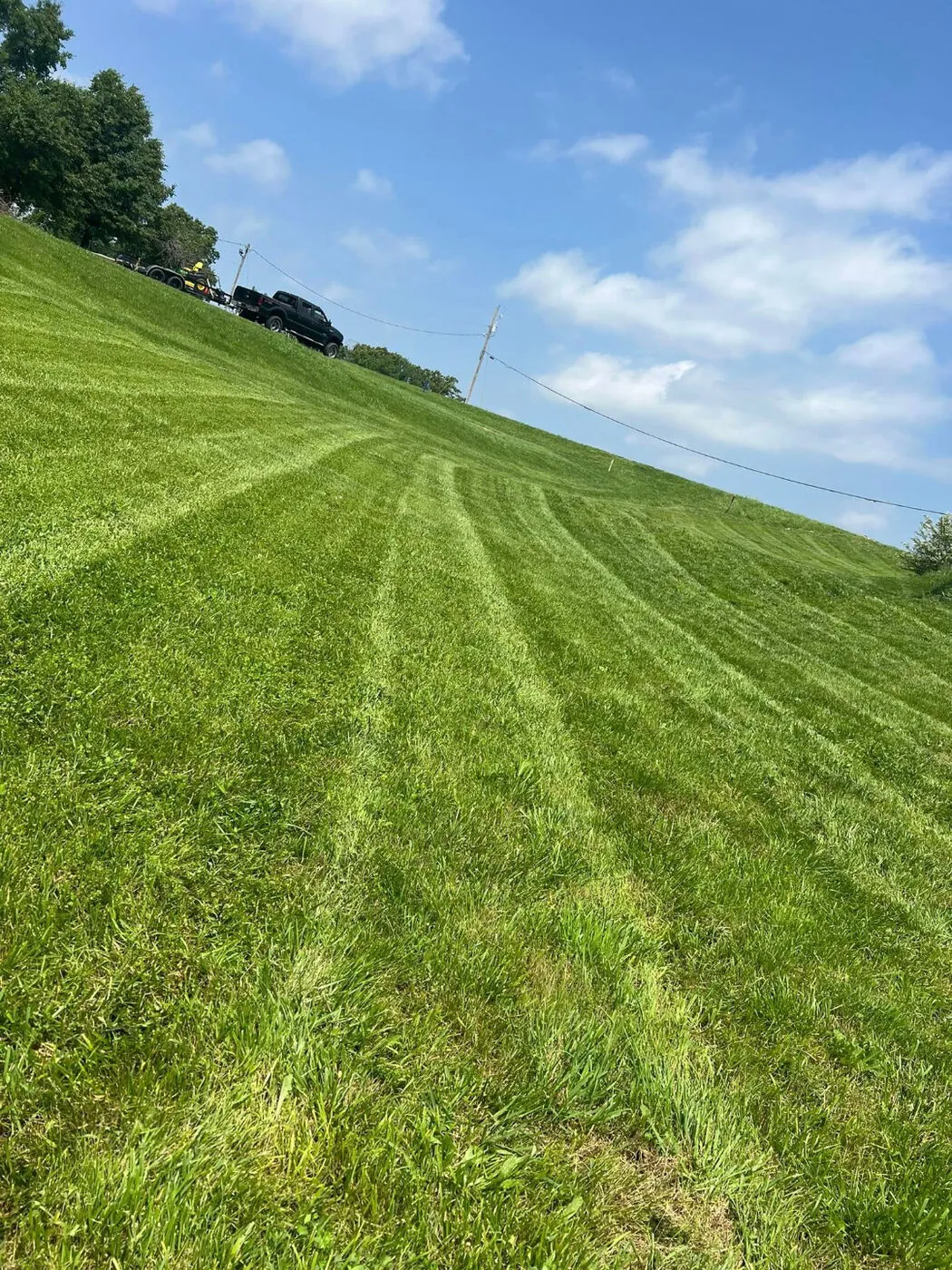 Freshly mowed hillside lawn with crisp, clean stripes under a bright blue sky.